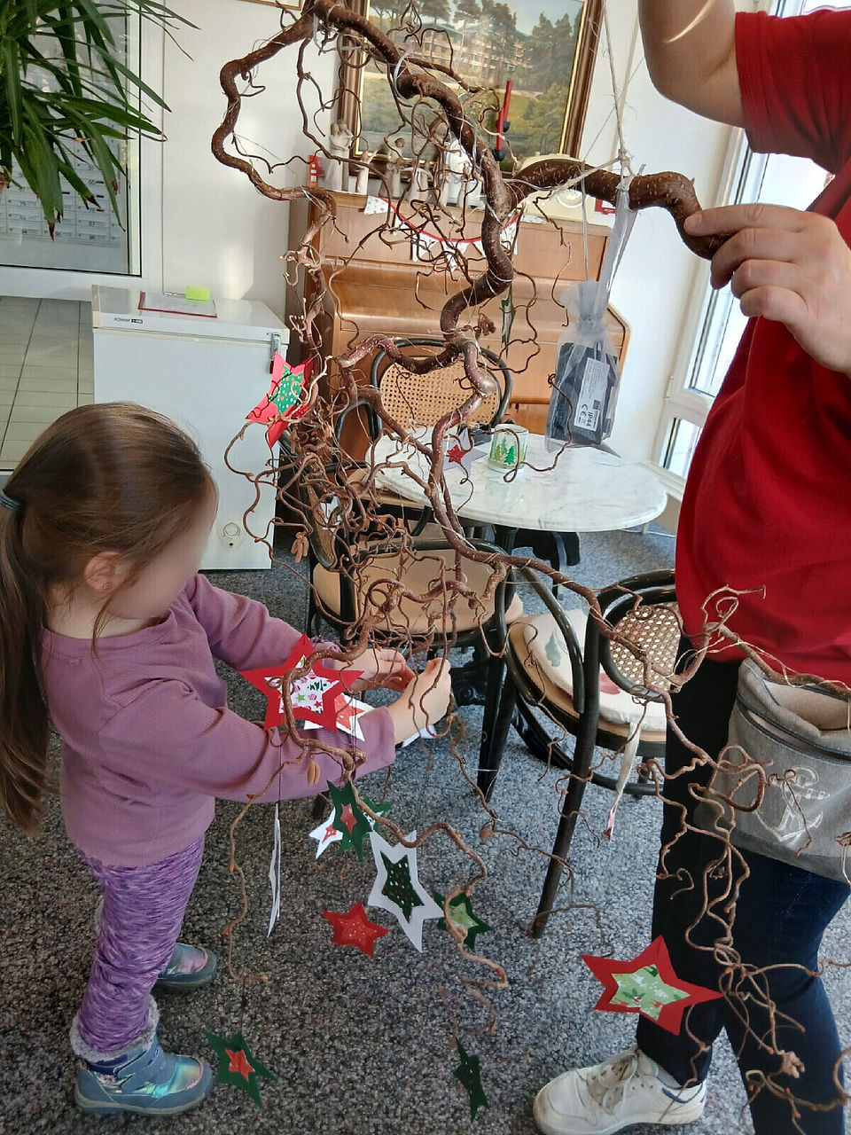 Eine kleine Helferin aus der DRK Kindertagesstätte Osterberg hängt selbst gebastelte Sterne an einen dekorativen Zweig.